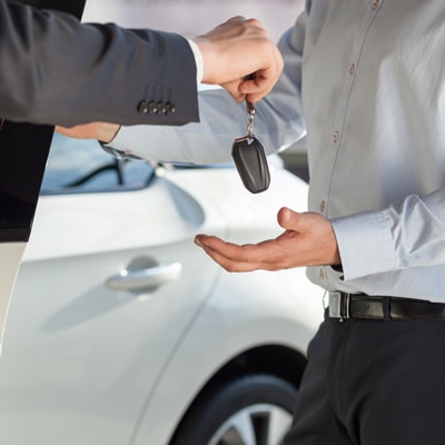 Man in a suit handing car keys back to someone after they restored their driver's license