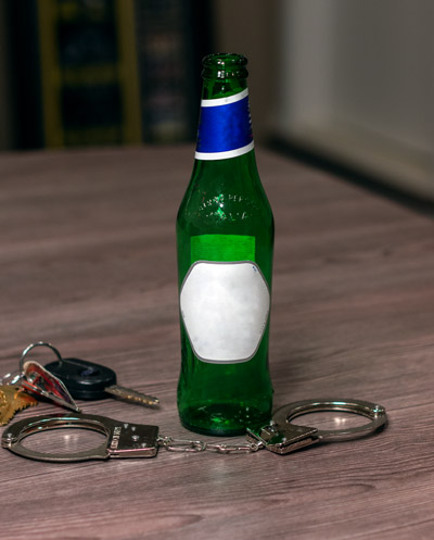 Empty bottle of alcohol on a table next to car keys and handcuffs symbolizing a possible OWI