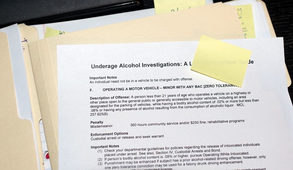 A page describing procedures and rules surrounding Michigans Zero Tolerance underage DUI law alongside a number of other documents inside multiple manila folders and post it notes