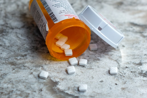 Open prescription drug container spilling unspecified white pills on a counter