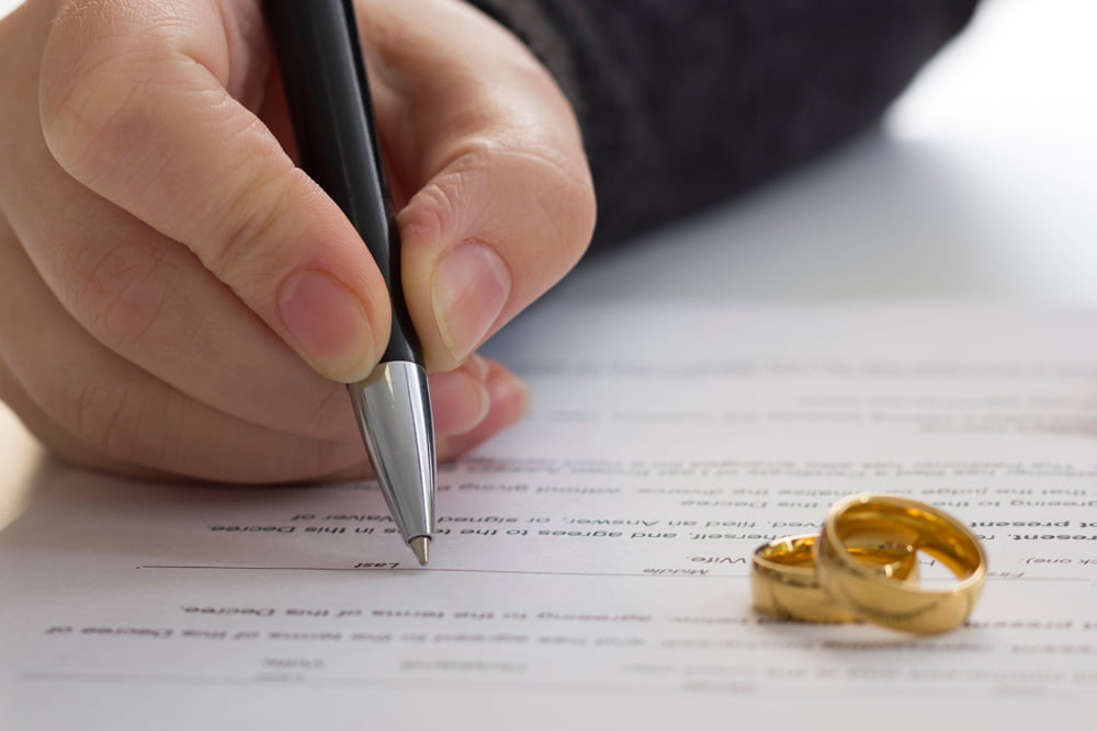 Divorce paper being signed with two wedding bands on the sheet