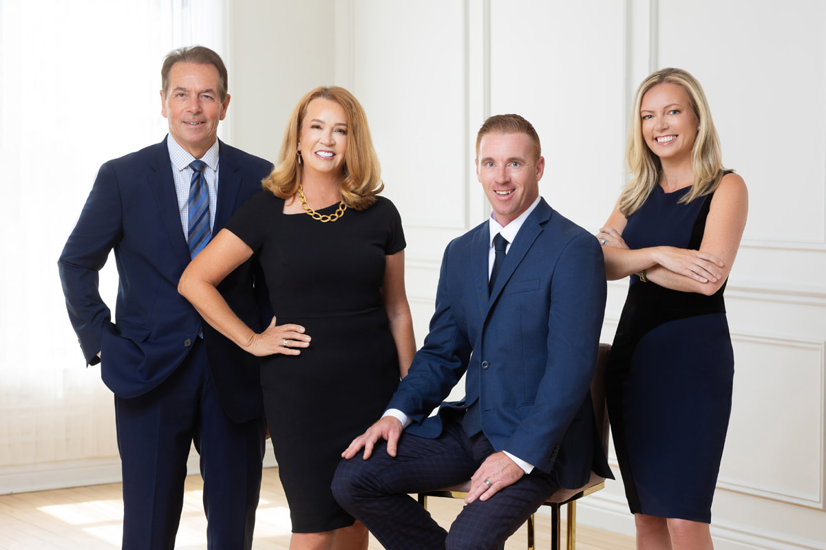 The Kelly family of Kelly & Kelly Law, group portrait in a bright office setting. From left to right: John Kelly, Michele Kelly, Mike Kelly, and Ryan Kelly, all dressed in professional attire